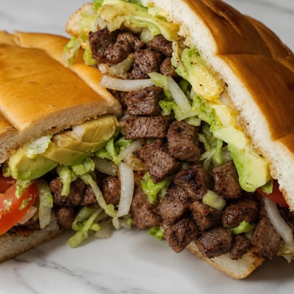A large torta sandwich, cut in half, filled with steak, lettuce, onions, tomatoes, and avocado.